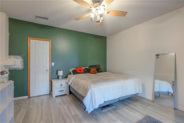 bedroom featuring a ceiling fan, a textured ceiling, visible vents, and light wood-style flooring