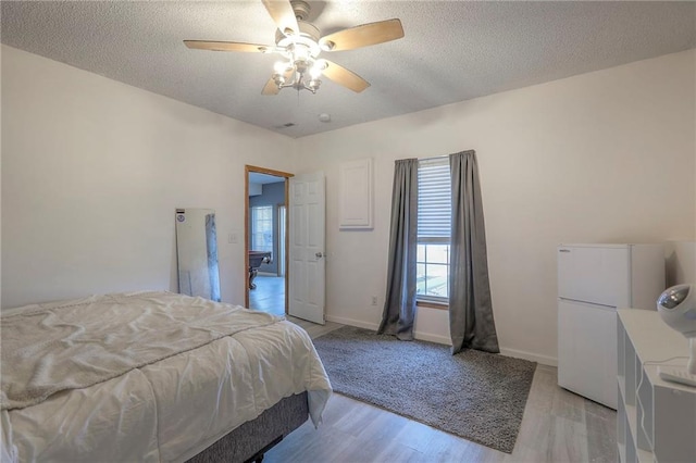 bedroom with a ceiling fan, a textured ceiling, baseboards, freestanding refrigerator, and light wood-style floors
