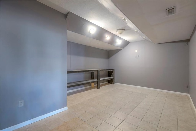 interior space featuring baseboards, light tile patterned flooring, lofted ceiling, and visible vents