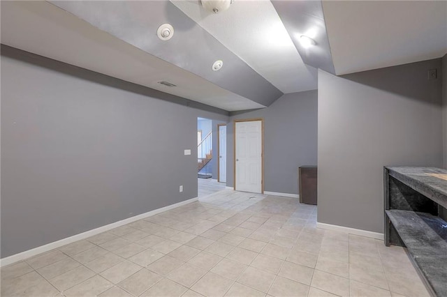 empty room with baseboards, visible vents, light tile patterned floors, and vaulted ceiling
