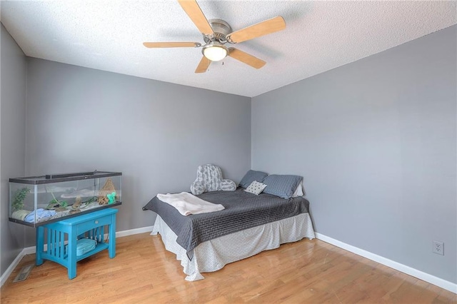 bedroom featuring baseboards, ceiling fan, a textured ceiling, and wood finished floors