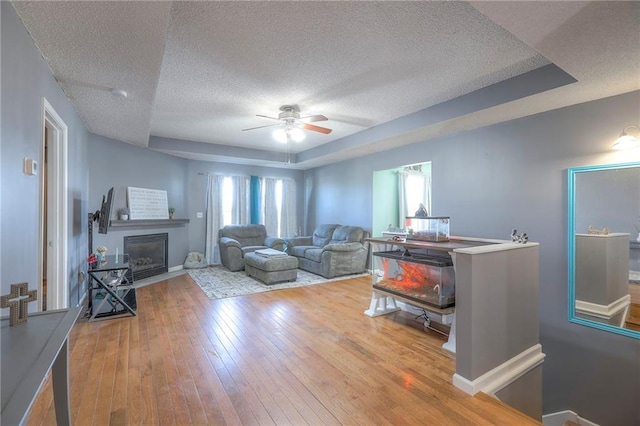 living room with a fireplace with flush hearth, hardwood / wood-style floors, ceiling fan, and a textured ceiling