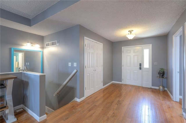 entryway featuring baseboards, light wood-type flooring, a textured ceiling, and visible vents