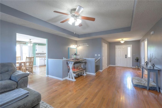 living room with a ceiling fan, a textured ceiling, visible vents, light wood-type flooring, and baseboards