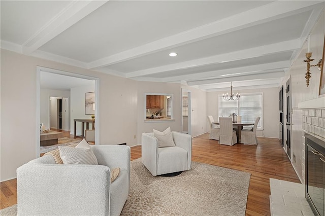 living area featuring beamed ceiling, wood finished floors, a chandelier, a brick fireplace, and recessed lighting