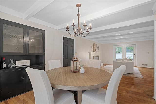 dining room with beamed ceiling, a chandelier, light wood-type flooring, a fireplace, and baseboards