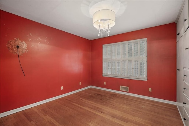 spare room with wood finished floors, a chandelier, and baseboards