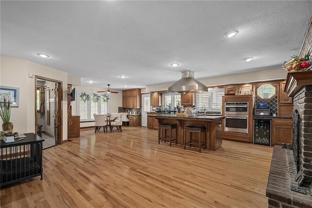 3705 W 119th Ter, Leawood, KS 66209 - kitchen featuring island exhaust hood, light wood-type flooring, a kitchen bar, stainless steel double oven, and a textured ceiling