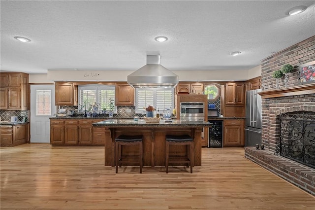 3705 W 119th Ter, Leawood, KS 66209 - kitchen with high end fridge, island exhaust hood, a breakfast bar area, a brick fireplace, and brown cabinets