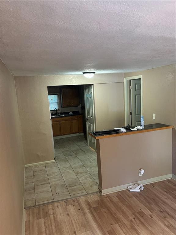 6941 Spruce Ave, Kansas City, MO 64132 - kitchen featuring a textured ceiling, light wood finished floors, dark countertops, and a peninsula