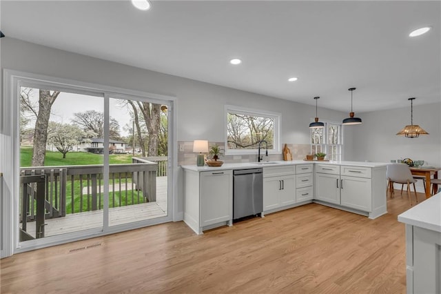 kitchen with light countertops, stainless steel dishwasher, a sink, light wood-style flooring, and a peninsula