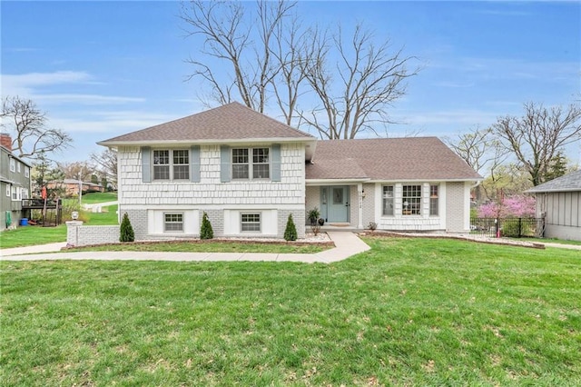 tri-level home featuring fence, roof with shingles, and a front lawn