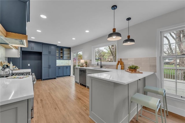kitchen featuring a peninsula, stainless steel appliances, a sink, light wood-style floors, and a kitchen breakfast bar