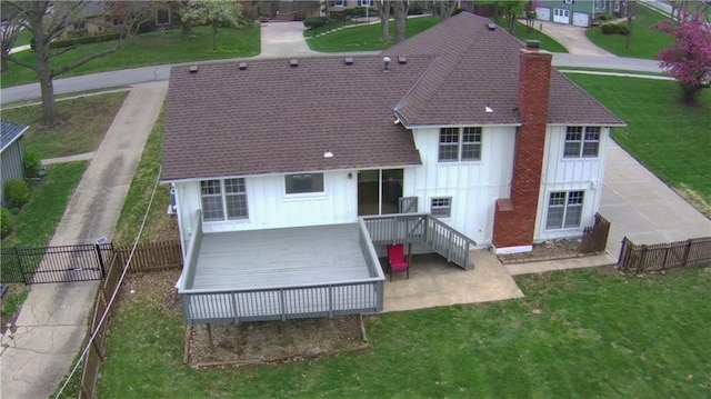back of property featuring fence, a wooden deck, board and batten siding, a yard, and a chimney