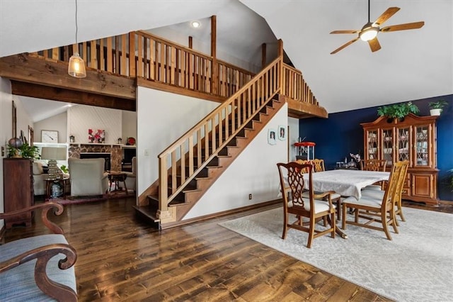 dining area featuring wood finished floors, stairs, a fireplace, high vaulted ceiling, and a ceiling fan