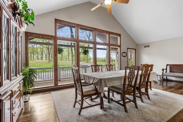 dining room with wood-type flooring, visible vents, ceiling fan, and high vaulted ceiling
