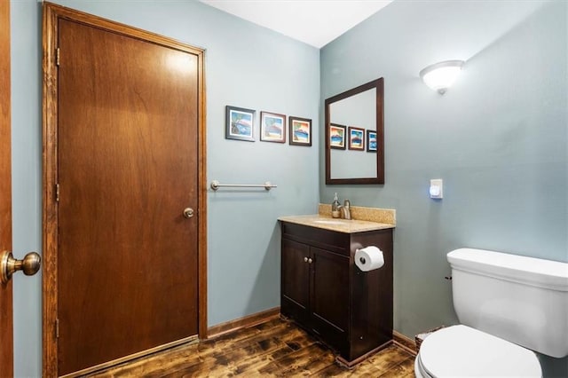 half bath featuring toilet, vanity, wood finished floors, and baseboards