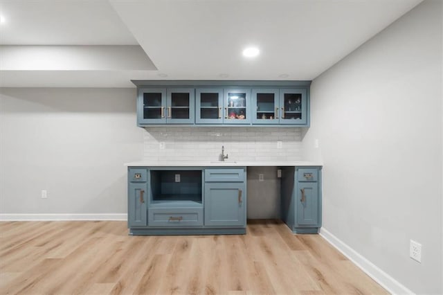 bar with light wood finished floors, a sink, decorative backsplash, and baseboards