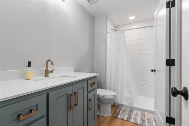 bathroom with visible vents, toilet, wood finished floors, vanity, and tiled shower