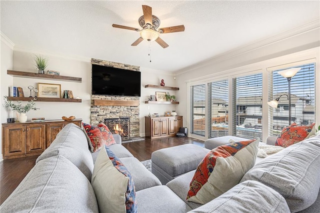 living room featuring a ceiling fan, a stone fireplace, dark wood finished floors, baseboards, and ornamental molding