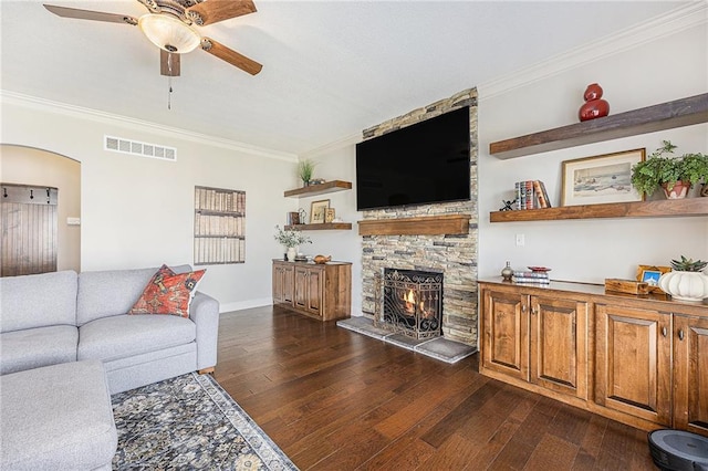 living area with crown molding, a stone fireplace, ceiling fan, dark wood finished floors, and visible vents