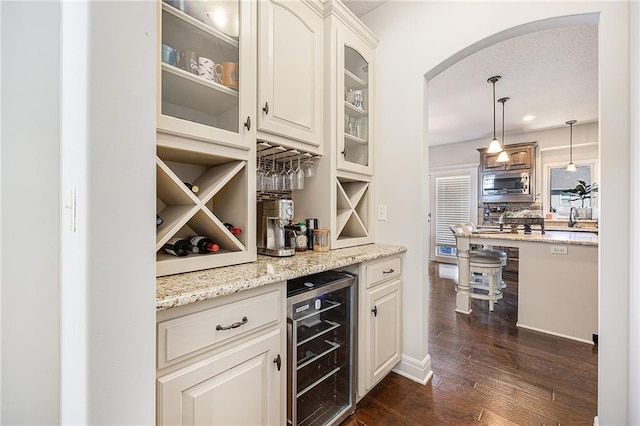 bar featuring beverage cooler, a dry bar, arched walkways, dark wood-type flooring, and tasteful backsplash