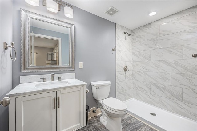 bathroom featuring a tile shower, toilet, baseboards, visible vents, and vanity