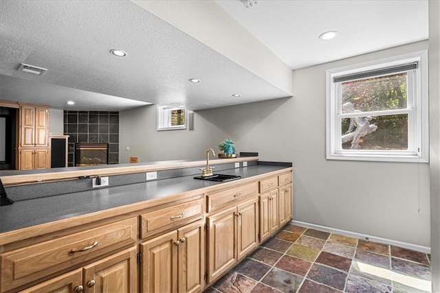 kitchen featuring dark countertops, visible vents, a sink, stone finish flooring, and baseboards