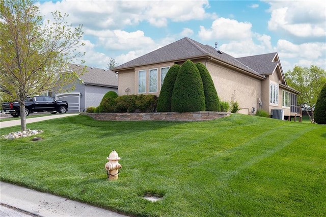 view of property exterior featuring central AC, concrete driveway, an attached garage, a yard, and stucco siding
