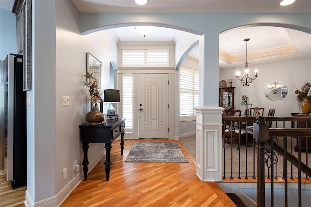 foyer with arched walkways, ornamental molding, light wood finished floors, and an inviting chandelier