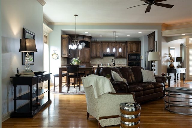 living area featuring ceiling fan with notable chandelier, arched walkways, ornamental molding, and dark wood finished floors
