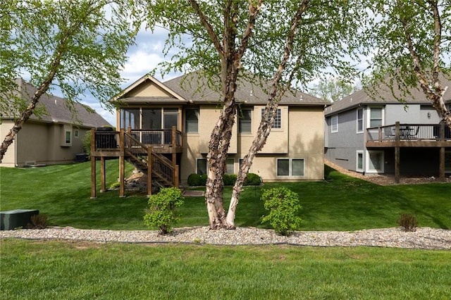rear view of house with a lawn, a deck, a sunroom, and stucco siding
