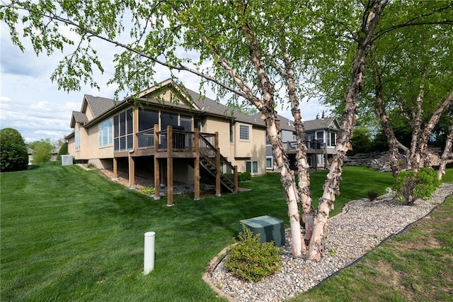 rear view of property with a wooden deck, stairway, a yard, a sunroom, and stucco siding