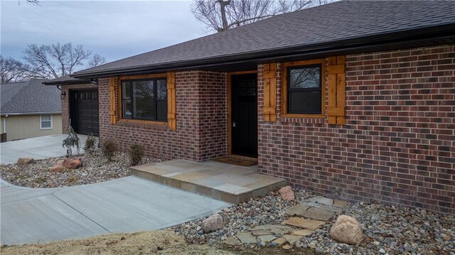 909 Bell Dr, Excelsior Springs, MO 64024 - property entrance featuring an attached garage, roof with shingles, brick siding, and concrete driveway