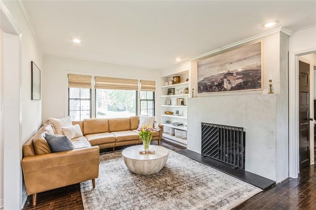 living area featuring built in shelves, a fireplace with raised hearth, dark wood-style floors, ornamental molding, and recessed lighting