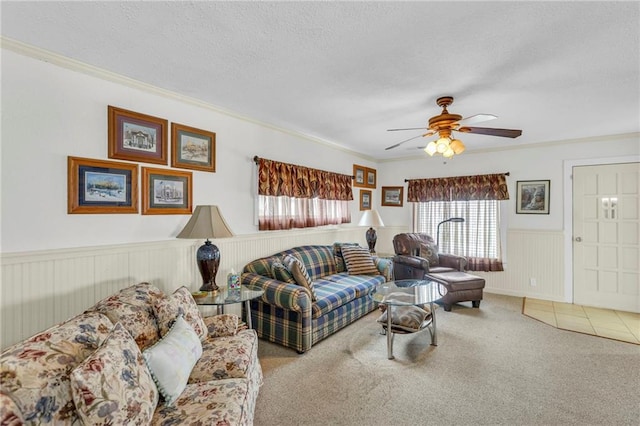 carpeted living area with crown molding, wainscoting, ceiling fan, and plenty of natural light