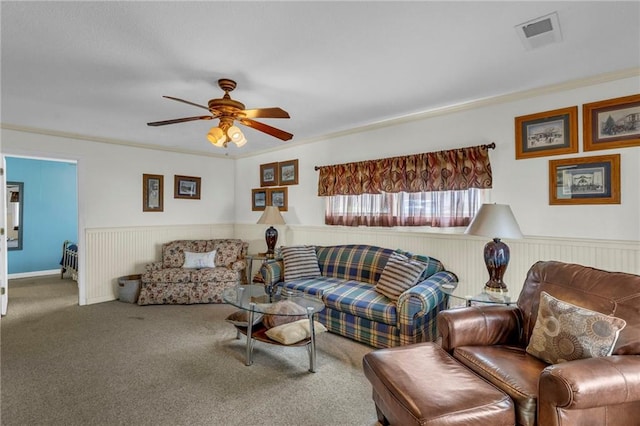 carpeted living area featuring a ceiling fan, visible vents, wainscoting, and ornamental molding
