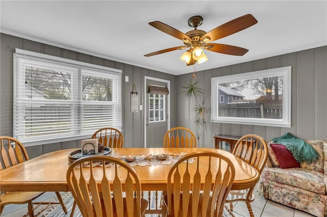 dining room with a ceiling fan, tile patterned floors, and a decorative wall