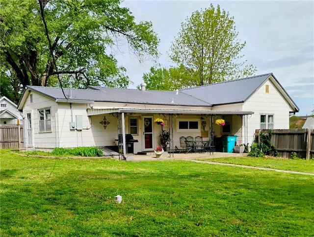 back of house featuring a patio, a lawn, fence, and metal roof