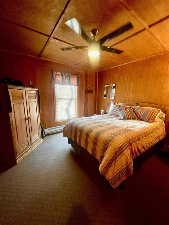 518 SW Lakeside Dr, La Cygne, KS 66040 - bedroom with wood walls, carpet, a baseboard heating unit, and ceiling fan