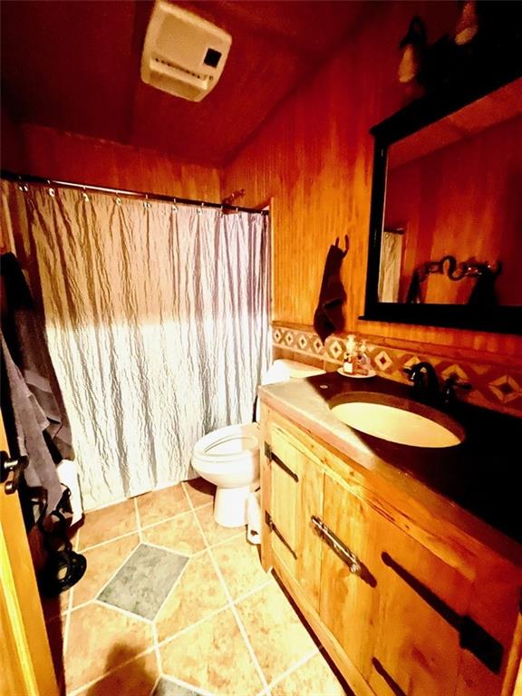 518 SW Lakeside Dr, La Cygne, KS 66040 - full bath featuring toilet, vanity, a wall mounted AC, wooden walls, and a shower with shower curtain