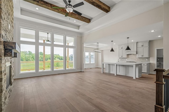 19389 W 114th Ter, Olathe, KS 66061 - unfurnished living room with ceiling fan, a raised ceiling, wood finished floors, beamed ceiling, and a fireplace