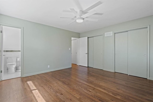 unfurnished bedroom featuring connected bathroom, multiple closets, a ceiling fan, wood finished floors, and visible vents