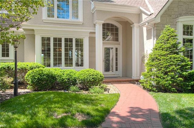 doorway to property featuring stucco siding, a lawn, and stone siding