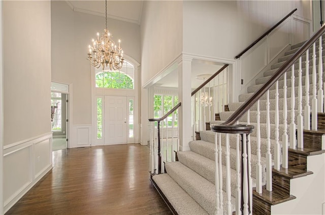 foyer entrance with a chandelier, a high ceiling, a decorative wall, crown molding, and wood finished floors