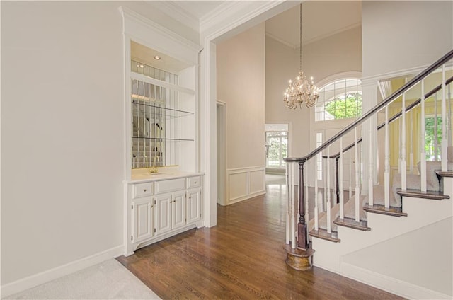 entryway with ornamental molding, stairs, a chandelier, dark wood finished floors, and a towering ceiling