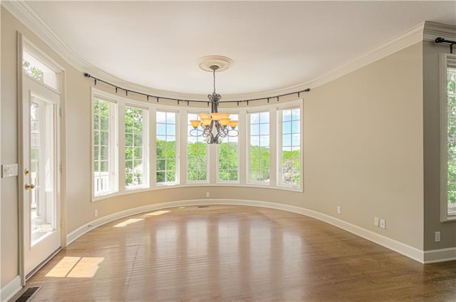 empty room featuring wood finished floors, crown molding, a chandelier, and baseboards