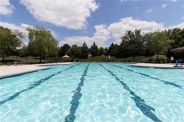 community pool with fence, a patio, and view of scattered trees