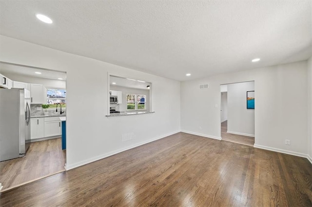 unfurnished living room featuring baseboards, recessed lighting, a textured ceiling, visible vents, and wood finished floors