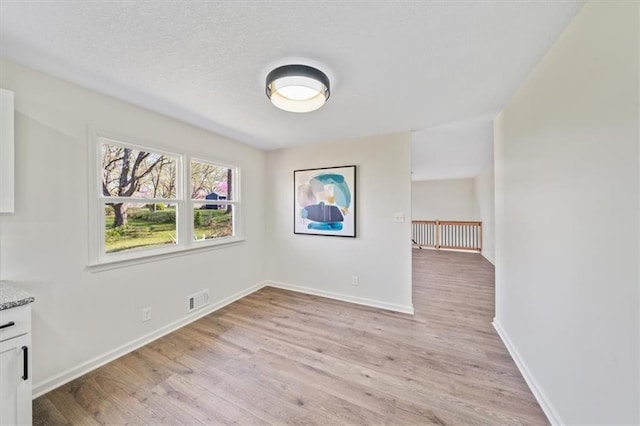 unfurnished dining area with light wood finished floors, visible vents, baseboards, and a textured ceiling